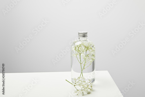 bottle with organic shampoo and wildflowers on white table on grey background