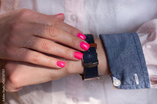 Manicured hand with pink nail and sleeve of shirt and hand watch