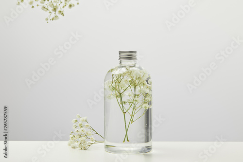 organic beauty product in transparent bottle with white wildflowers on grey background