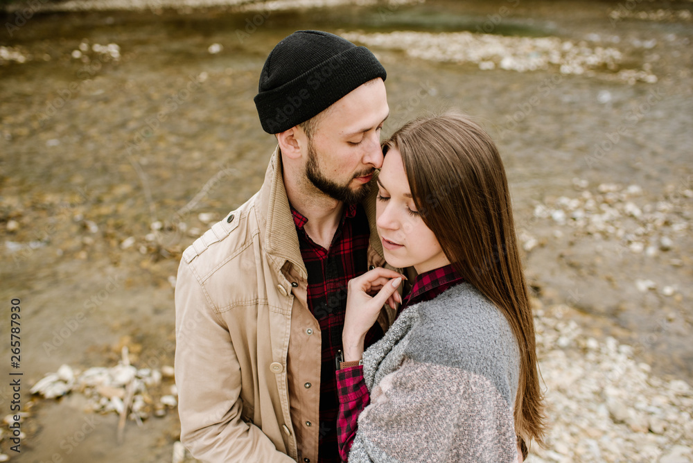 Fototapeta premium Young travelers couple hugs each other on the mountain river on the background