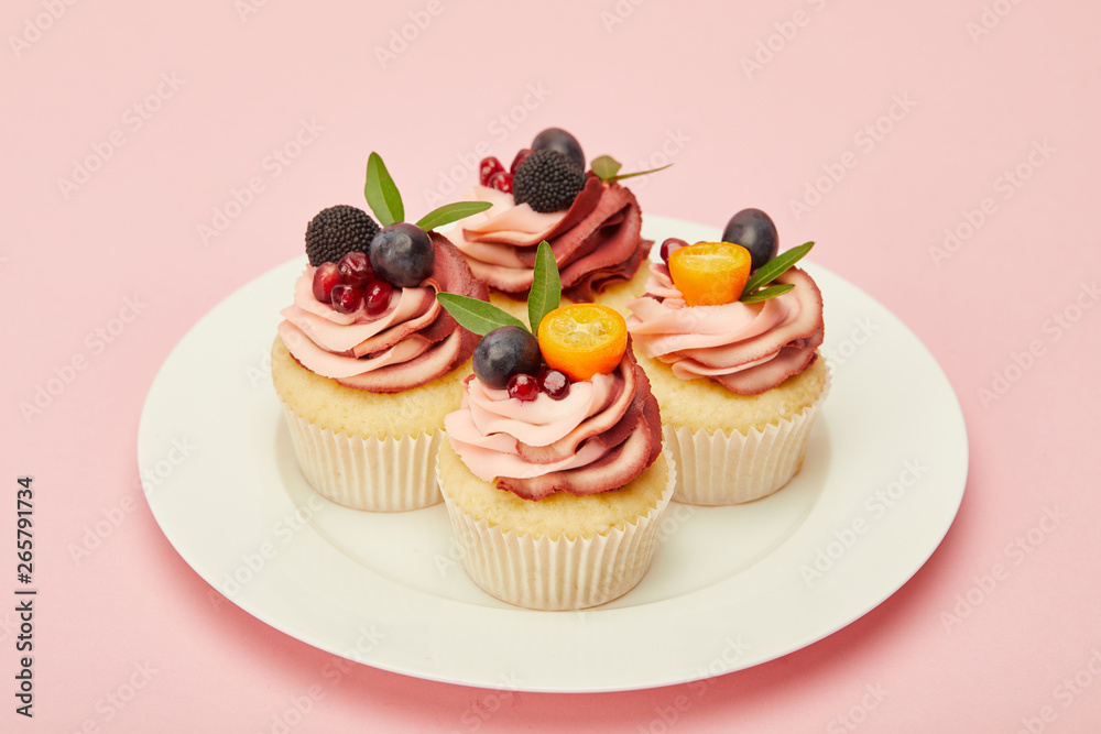 sweet cupcakes with berries and fruits on plate on pink surface