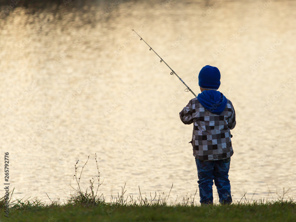 The boy catches fish on the pond at sunset The boy catches fish on the pond at sunset