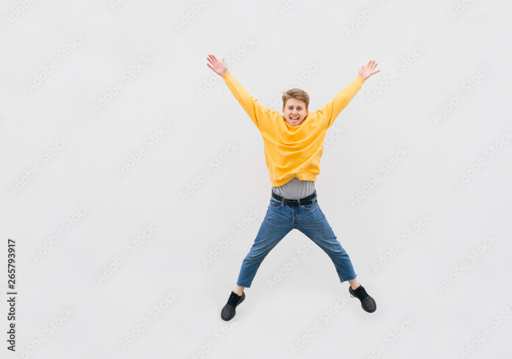 Happy guy in Casual clothes jumps against the background of a white wall, street portrait. Young man is leap on the background of a white wall,jumping on the street, isolated. Copyspace