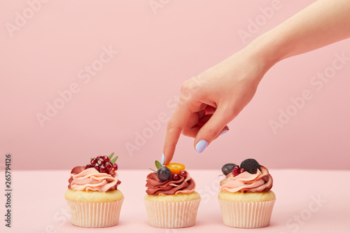 cropped view of woman with sweet cupcakes with fruits and berries isolated on pink