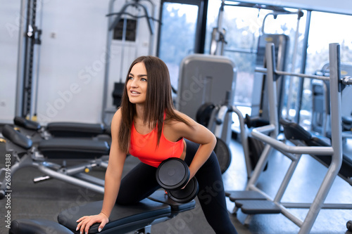 slim woman exercis with dumbbells on bench at gym