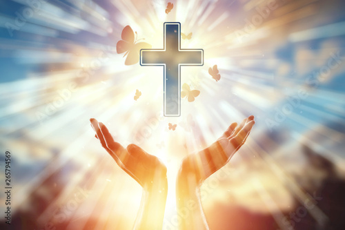 Close-up hands on the background of the symbol of Christian, prayer, catholic cross, a flock of butterflies flies. Christian religion, the concept of hope, faith, religion