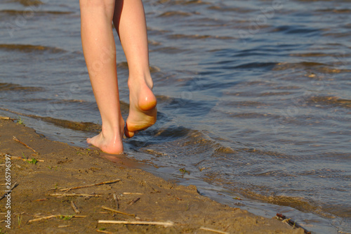 The child walks along the sandy shore of the pond. Feet close up.