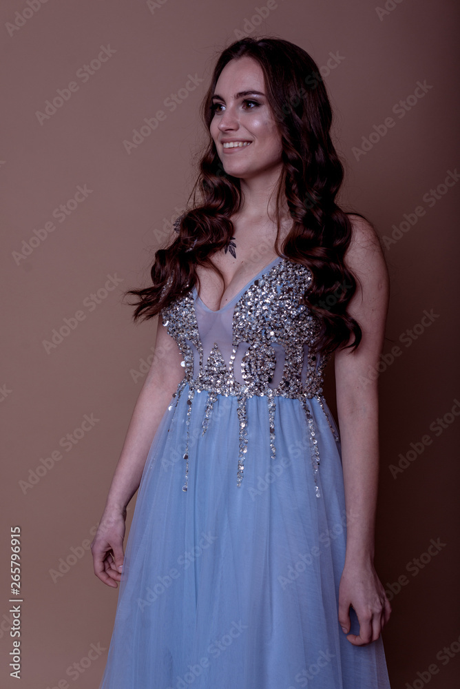Beautiful young girl in a flying blue dress with sequins and embroidery. Flowing fabric. bride in a white dress on a beige background. gorgeous brunette on a studio background. Isolate.girl on a brown Beautiful young girl in a flying blue dress with sequins and embroidery. Flowing fabric. bride in a white dress on a beige background. gorgeous brunette on a studio background. Isolate.girl on a brown