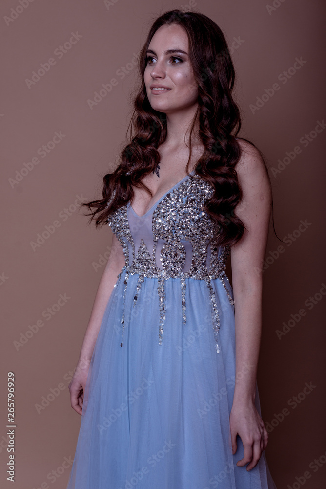 Beautiful young girl in a flying blue dress with sequins and embroidery. Flowing fabric. bride in a white dress on a beige background. gorgeous brunette on a studio background. Isolate.girl on a brown Beautiful young girl in a flying blue dress with sequins and embroidery. Flowing fabric. bride in a white dress on a beige background. gorgeous brunette on a studio background. Isolate.girl on a brown