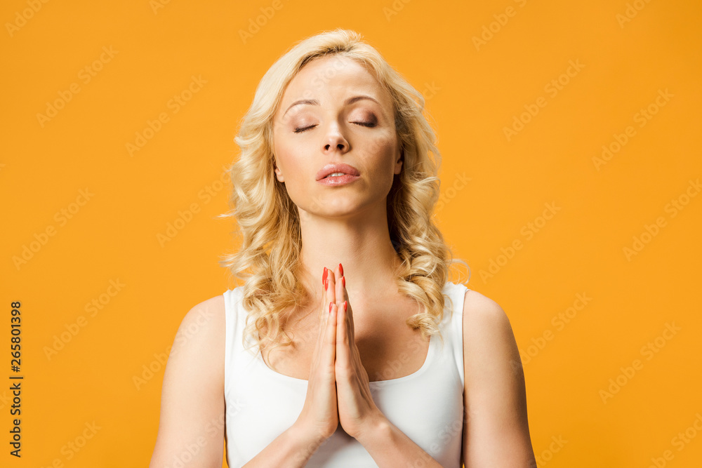 blonde woman standing with praying hands isolated on orange