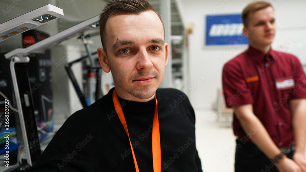 Portrait of best a Professional Expert Consultant Smiles and Looks into Camera as Stands in the Bright, Modern Electronics Store Full of Latest Models of TV Sets, Cameras, Tablets and other Devices. Portrait of best a Professional Expert Consultant Smiles and Looks into Camera as Stands in the Bright, Modern Electronics Store Full of Latest Models of TV Sets, Cameras, Tablets and other Devices.