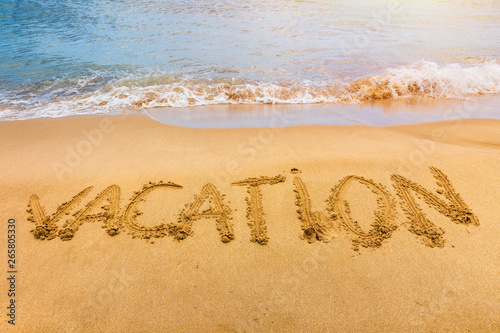 Vacation text on a beach. Vacation written in a sandy tropical beach.  Vacation  written in the sand on the beach blue waves in the background. Vacation on the sand beach concept.