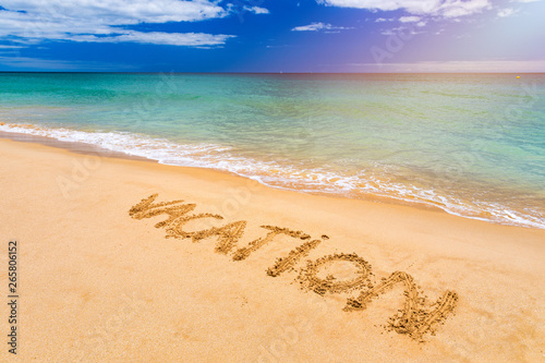 Vacation text on a beach. Vacation written in a sandy tropical beach.  Vacation  written in the sand on the beach blue waves in the background. Vacation on the sand beach concept.