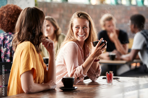 Two Female Friends Sitting At Table In Coffee Shop And Talking