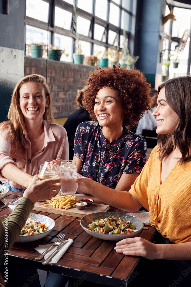 Four Young Female Friends Meeting For Drinks And Food Making A Toast In Restaurant