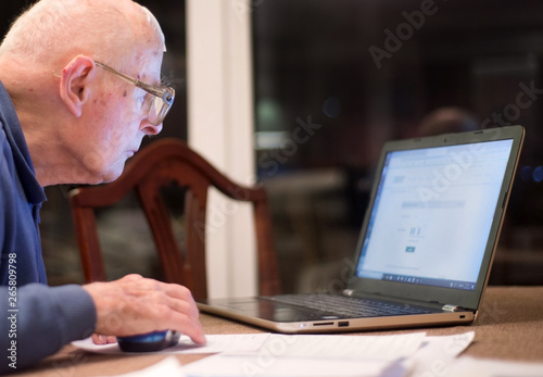 Elderly man using a laptop computer ,checking his share portfolios ,Hampshire,England,U.K. photo