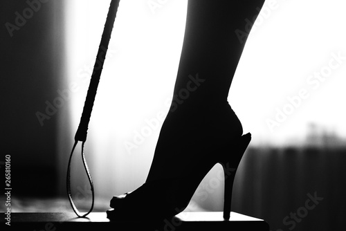 sexy woman leg and ridding crop. woman domination and foot fetish. sexy woman leg in high heel mules. photo