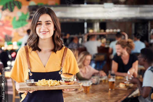 Portrait Of Waitress Serving Food To Customers In Busy Bar Restaurant photo