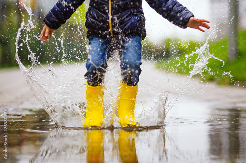 Canvas Print legs of child with yellow rubber boots jump in puddle on an autumn walk
