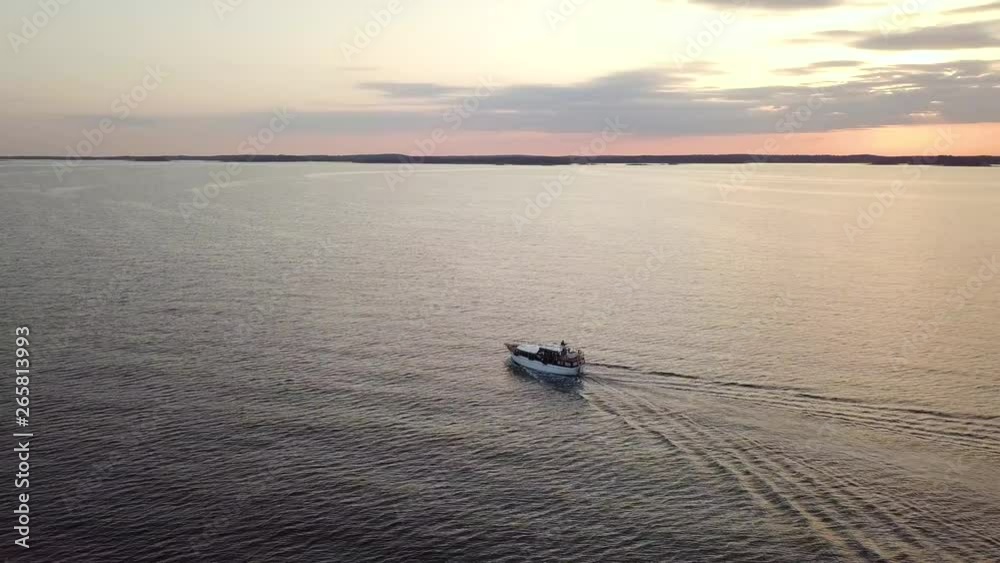 A SLOW CIRCLING AERIAL VIEW of a boat travelling on the sea at sunset. TRACKING SHOT. A SLOW CIRCLING AERIAL VIEW of a boat travelling on the sea at sunset. TRACKING SHOT.