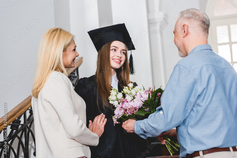happy father giving flowers to cheerful daughter in graduation cap ...