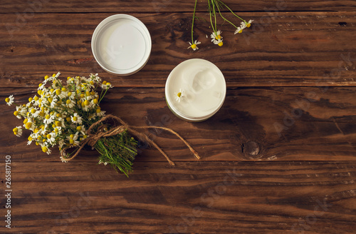 Chamomile bouquet and fragrant body cream on a wooden table