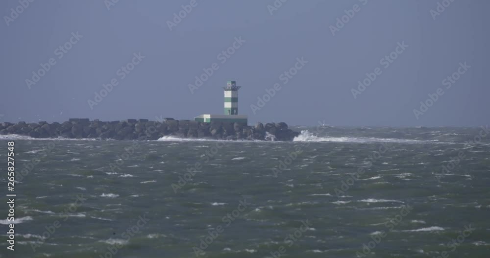 Stormy day atthe pier, lightstand with huge waves breaking on breakwater, windforce 8 bft, green white lightstand. Stormy day atthe pier, lightstand with huge waves breaking on breakwater, windforce 8 bft, green white lightstand.