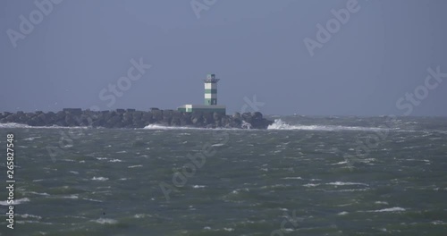 Stormy day atthe pier, lightstand with huge waves breaking on breakwater, windforce 8 bft, green white lightstand. photo