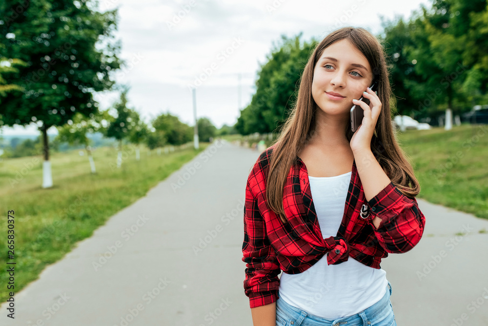 Girl schoolboy in a red shirt, in the summer in city stands on the road. Calls to parents and girlfriends. Online application to Internet. Long hair mug with tea. Free space for text.