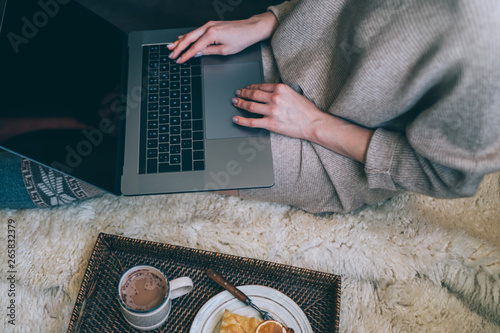 Christmas online shopping. Woman buys presents, prepare to xmas eve. Female with laptop, copy space on screen. Hot coffee, spice and almond cakes on tray. Cozy blanket. Toned image. Soft focus.