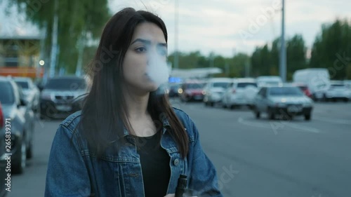 Serious cute girl vaping on the parking near the mall