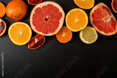 Top view. Sliced colorful citrus on a black background. Copy space. Fruits are laid out on top.