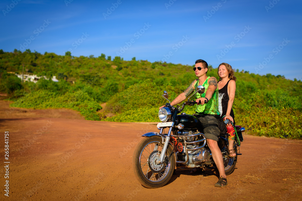 Young beautiful couple hipsters in stylish clothing on the motorcycle posing against a blue sky and green grass. Adventure and vacations concept.