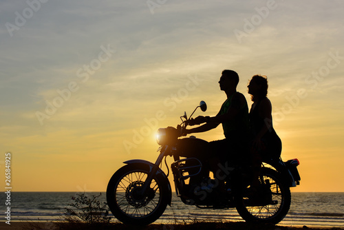 Silhouettes of guy and girl on motorcycle on sunset background. Young couple are sitting on motorcycle  faces in profile.