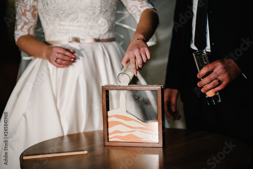 Wedding ceremony, mixing sands is a new family.  Close up view hands of bride and groom doing sand ceremony during wedding. Newlyweds, nice young couple.