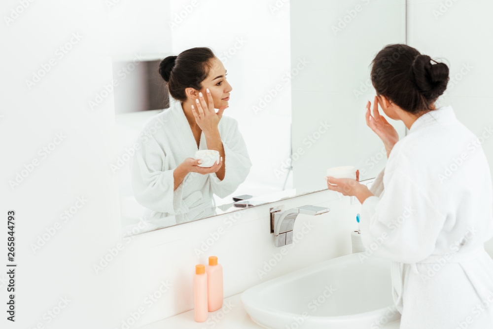 selective focus of attractive woman applying face cream while looking at mirror selective focus of attractive woman applying face cream while looking at mirror