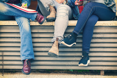 Legs of students sitting on a bench.