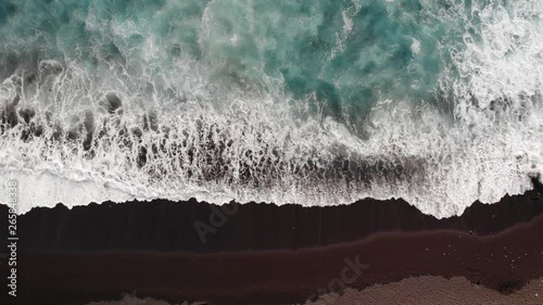 Areial view of blue waves crashing into the black sand beach