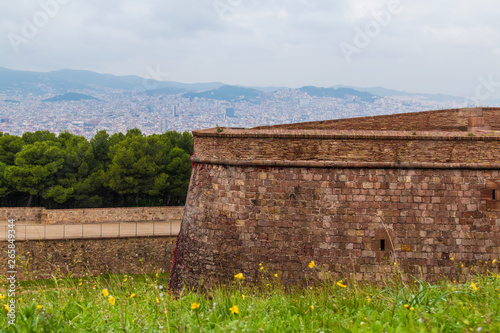 The stone wall of the Montjuic Castle on the background of the Bacelona city in overcast day, Spain photo