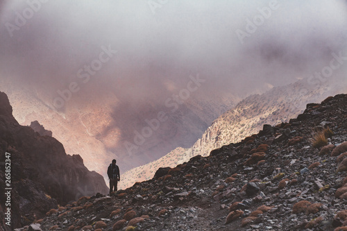 einsamer Wanderer in den Bergen des Atlas Gebirges, der in eine Schlucht voll mit Nebel schaut. photo