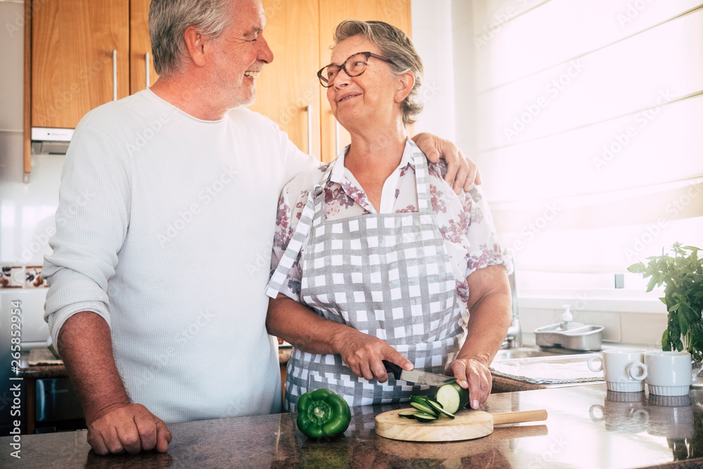 Happy old senior retired beautiful white hair couple of people cooking together at home in the kitchen cutting vegetables for healthy food lifestyle concept