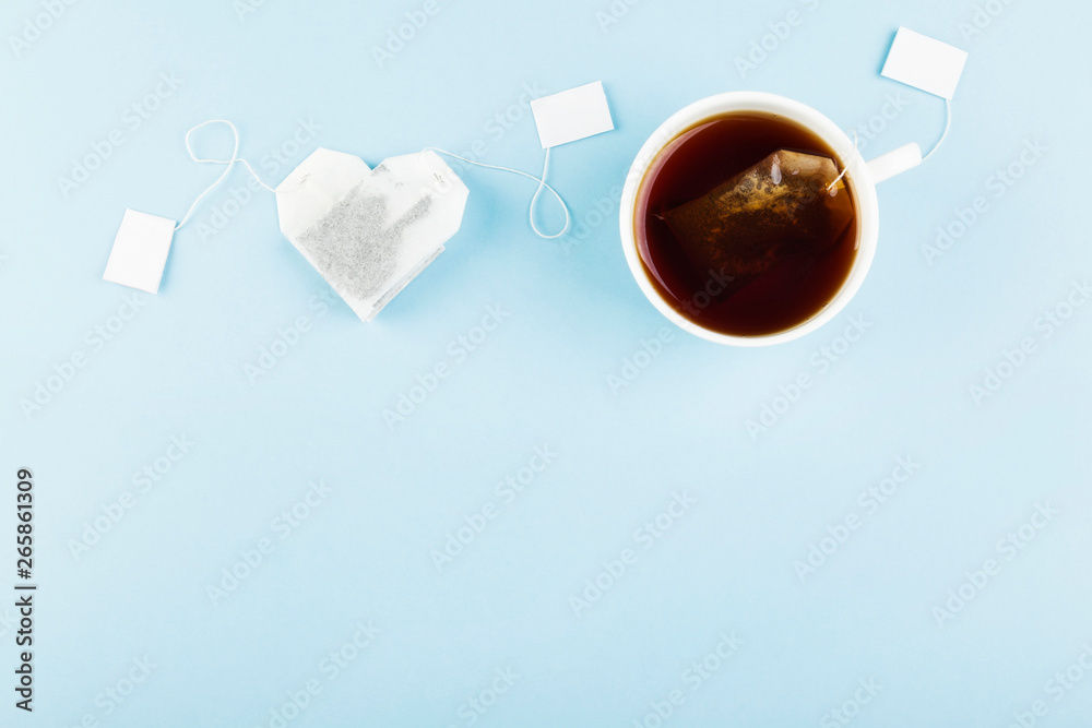 Cup of tea and tea bags in form of heart on blue background. Top view, copy space. Food background - obrazy, fototapety, plakaty 