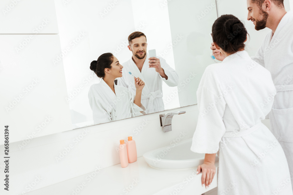 selective focus of cheerful man taking photo with happy woman holding toothbrush selective focus of cheerful man taking photo with happy woman holding toothbrush