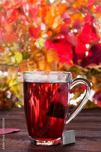 Hot drink with hibiscus red tea teabag in glass on wooden background