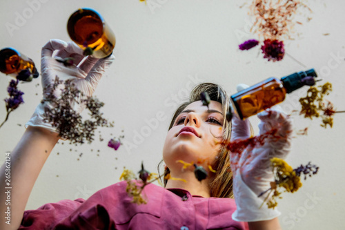 Young woman perfumer preparing herbs and flowers for make a perfume. Under table view.