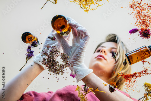 Young woman perfumer preparing herbs and flowers for make a perfume. Under table view.