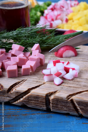 Process of making Okroshka soup. Chopping radish  sausage and other ingredients on wooden cutting board