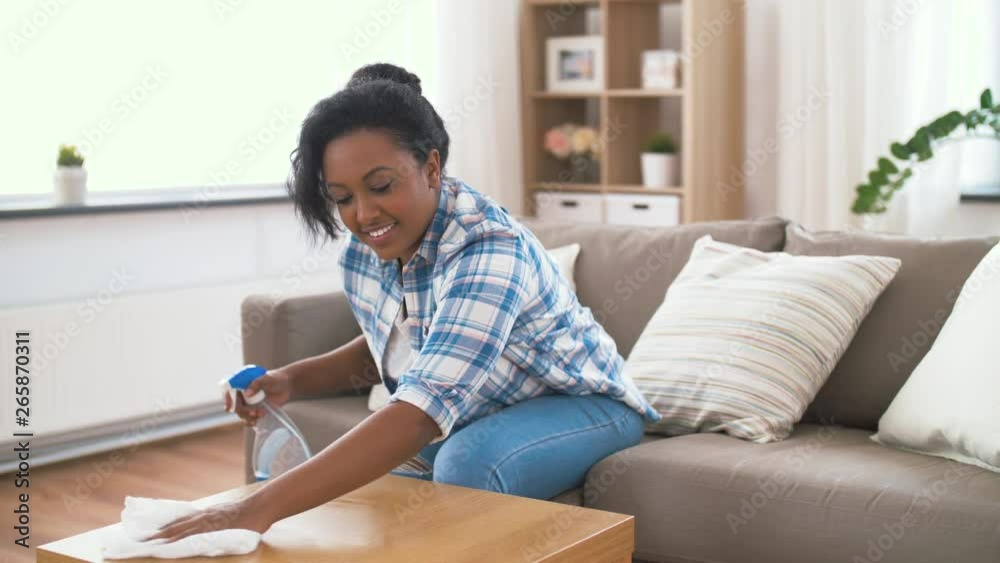 household, cleaning and people concept - happy african american woman or housewife with spray detergent wiping table by paper tissue or rag at home household, cleaning and people concept - happy african american woman or housewife with spray detergent wiping table by paper tissue or rag at home