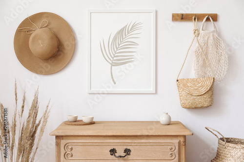 Stylish korean interior of living room with brown mock up poster frame, elegant accessories, flowers, wooden shelf and hanging rattan bags and hat. Minimalistic concept of home decor. Template.  photo