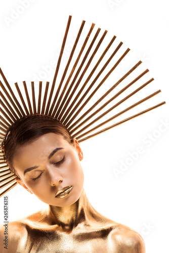 nude young woman painted in golden with big accessory on head and closed eyes isolated on white
